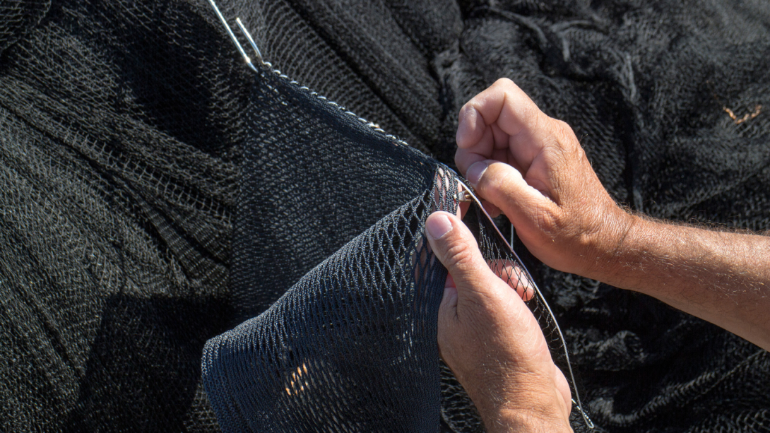 primer plano de unas manos cosiendo una red de pesca